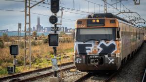 Un tren transita por la R1 de Rodalies, con las Tres Xemeneies de Sant Adrià al fondo