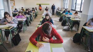 Alumnos y alumnas de secundaria, realizando un examen en clase bajo la supervisión de su profesor.